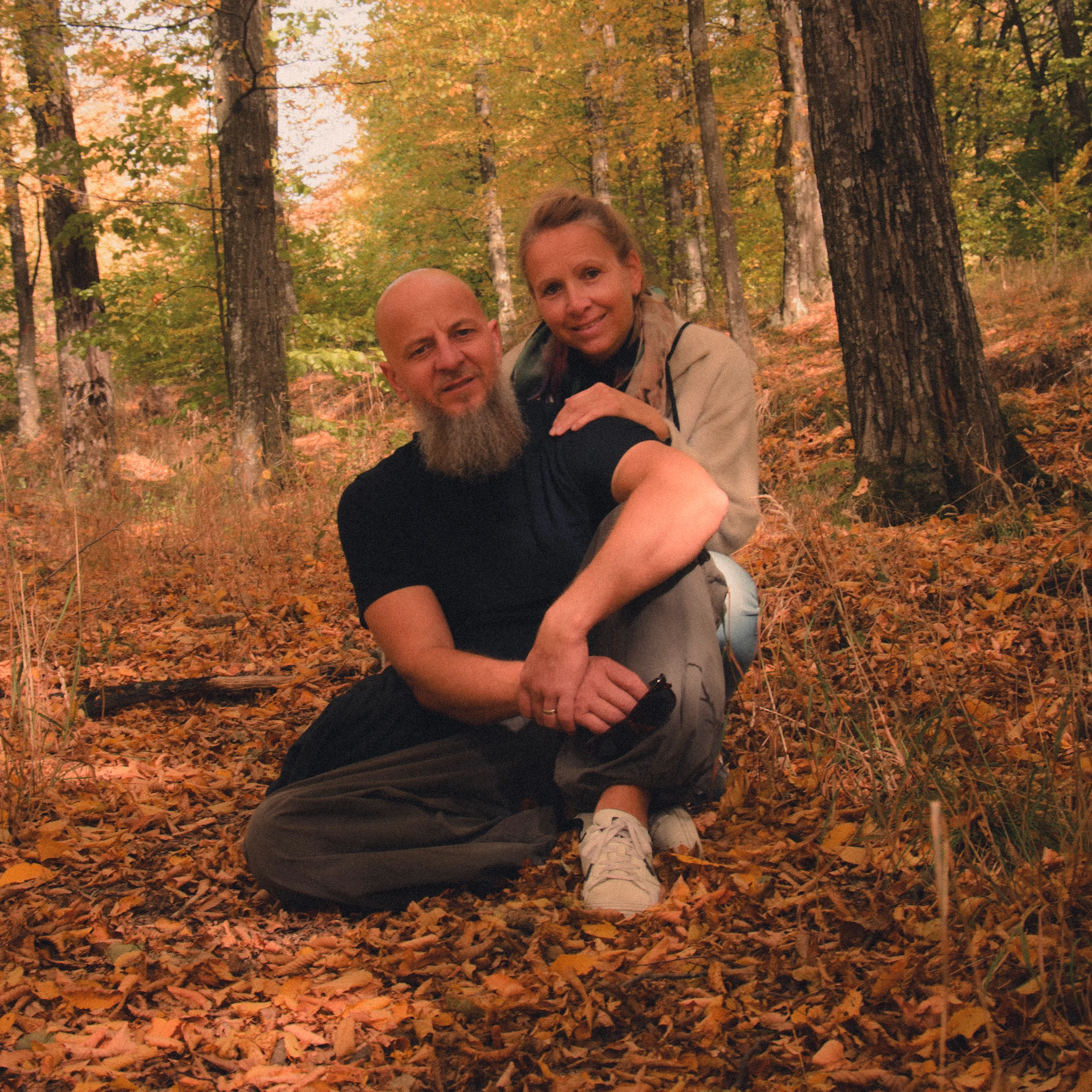 Two people sitting by a tree among autumn leaves