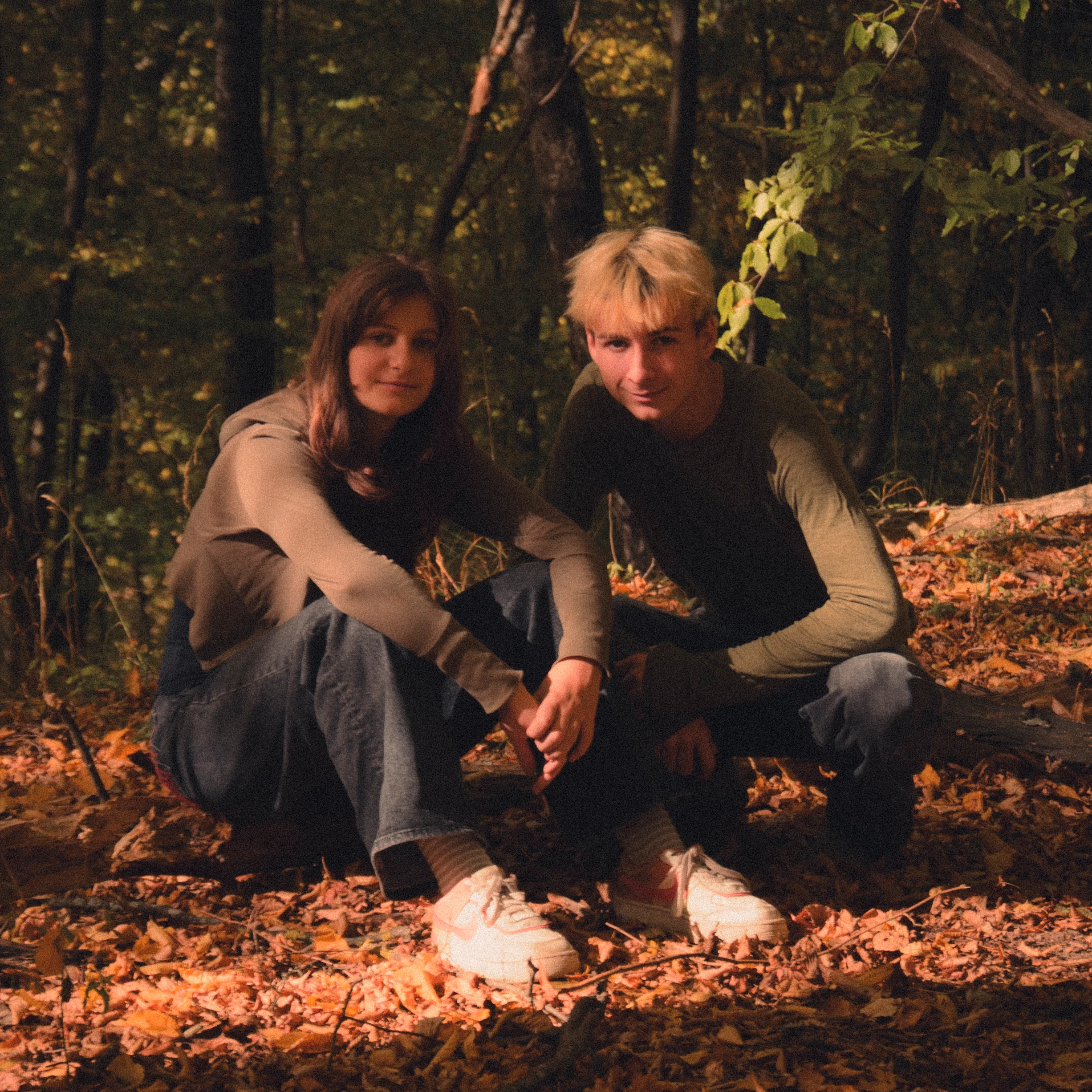 Two people crouching together among fallen leaves